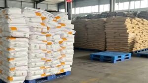Factory warehouse bulk stock of Riboflavin-5'-Phosphate Sodium Dihydrate FMN-Na, stacked 25kg export packaging bags on blue plastic pallets, large supply capacity for global buyers